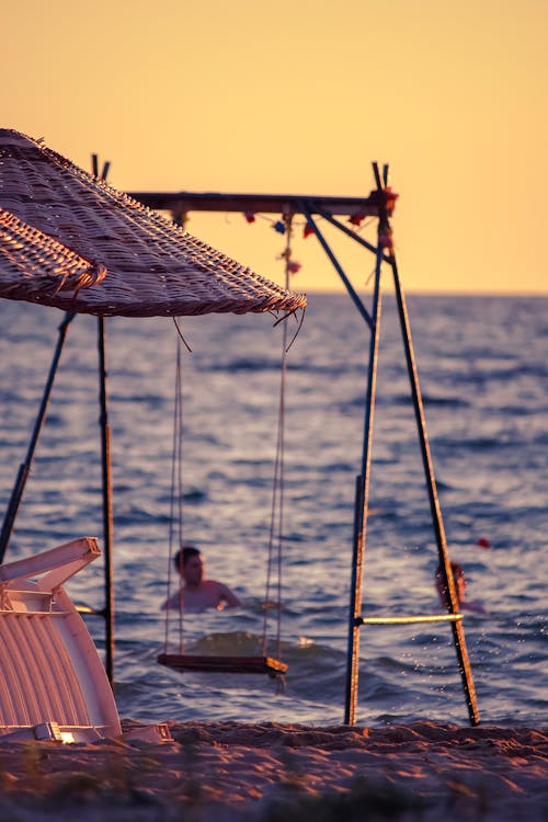 A Swing on the Beach and Man Swimming in the Water at Sunset 