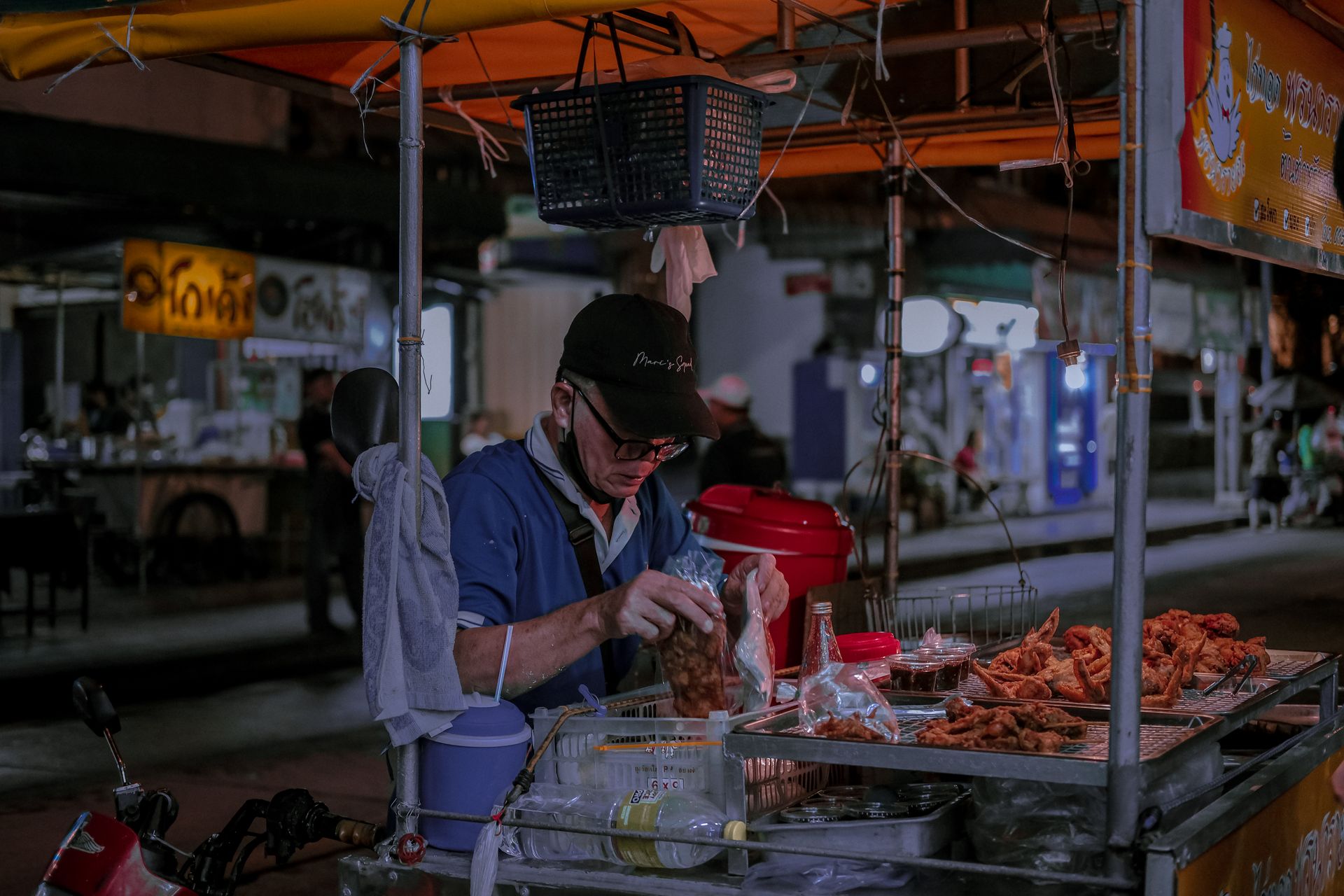 A street vendor packages fried snacks at a vibrant night market stall.