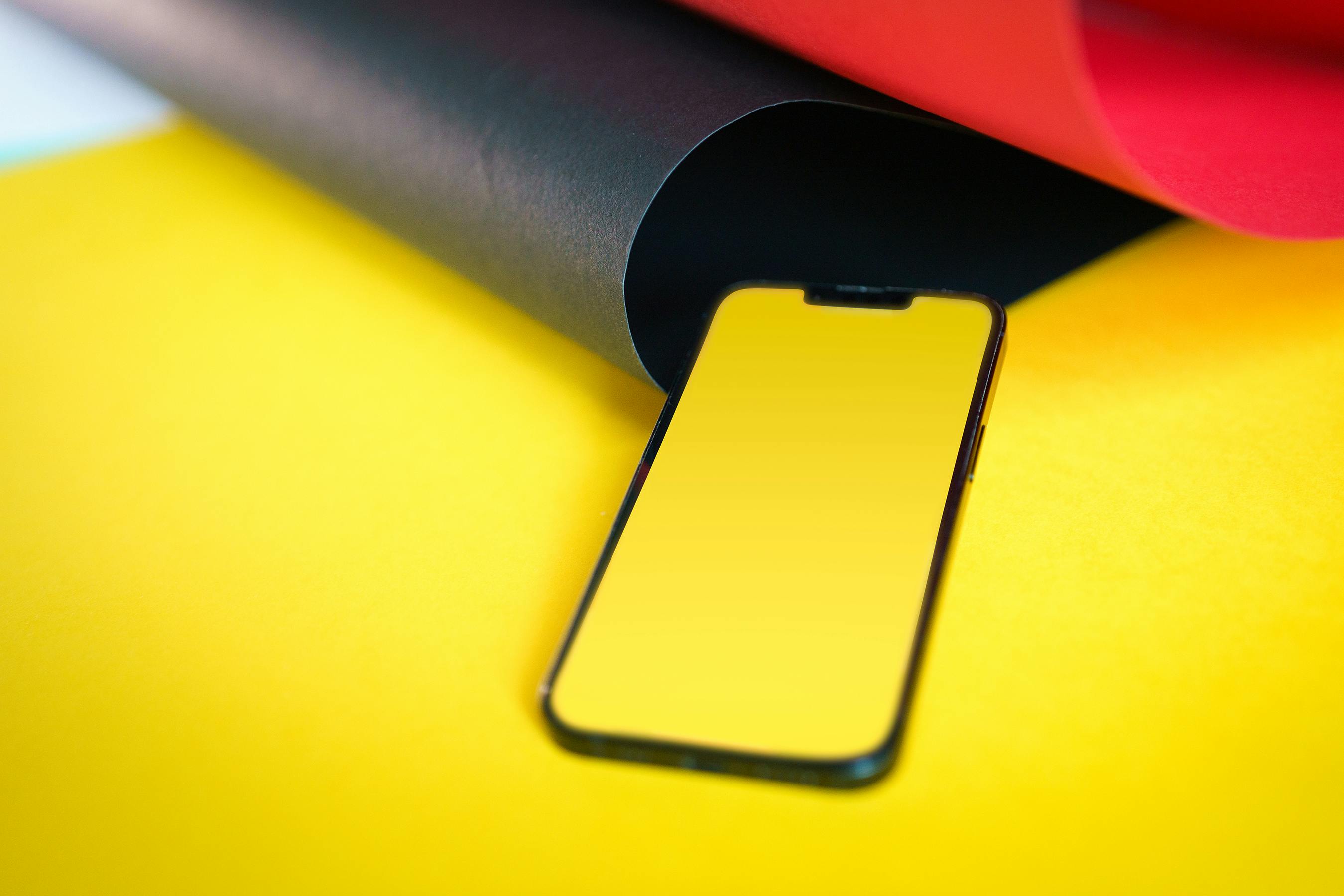 Smartphone with blank screen on red, black, and yellow paper background.