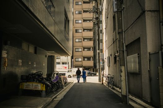 A narrow urban alley with bicycles and pedestrians walking towards a city street.