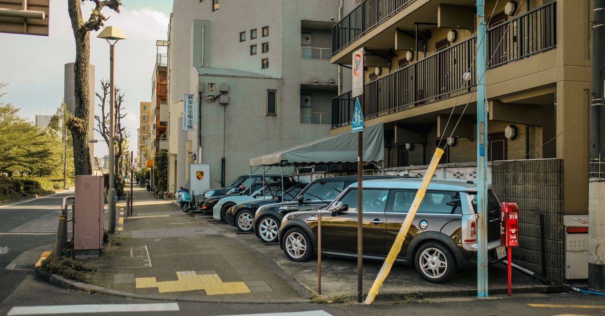 A street view capturing parked cars alongside residential buildings on a sunlit day.