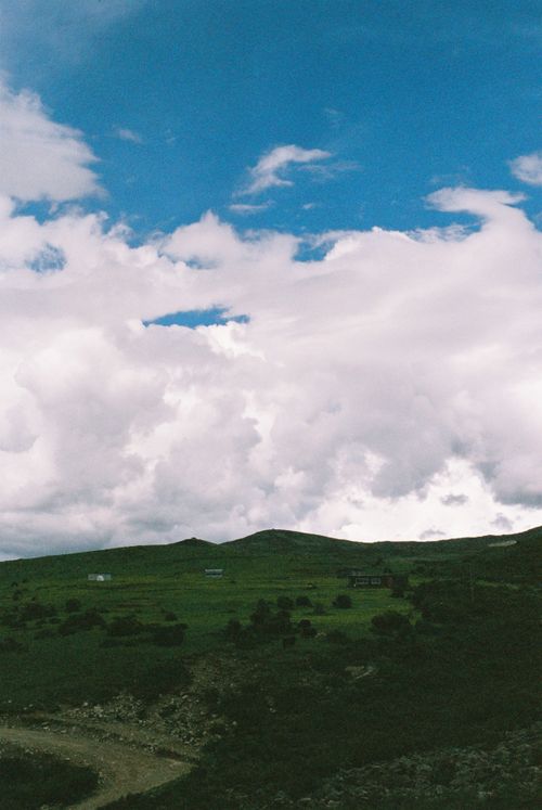 Free A picturesque view of rolling green hills under a vibrant sky with white clouds. Stock Photo