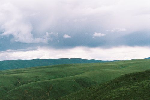 Free Expansive green hills with a dramatic cloudy sky, showcasing tranquil rural landscape. Stock Photo
