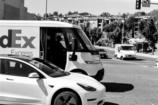 A black and white urban street scene featuring vehicles including a delivery van and a modern car.
