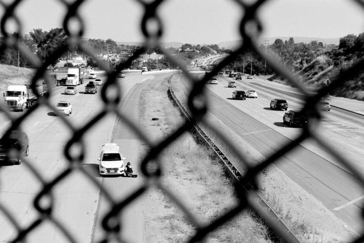 View Behind Fence On Cars Driving On Highway