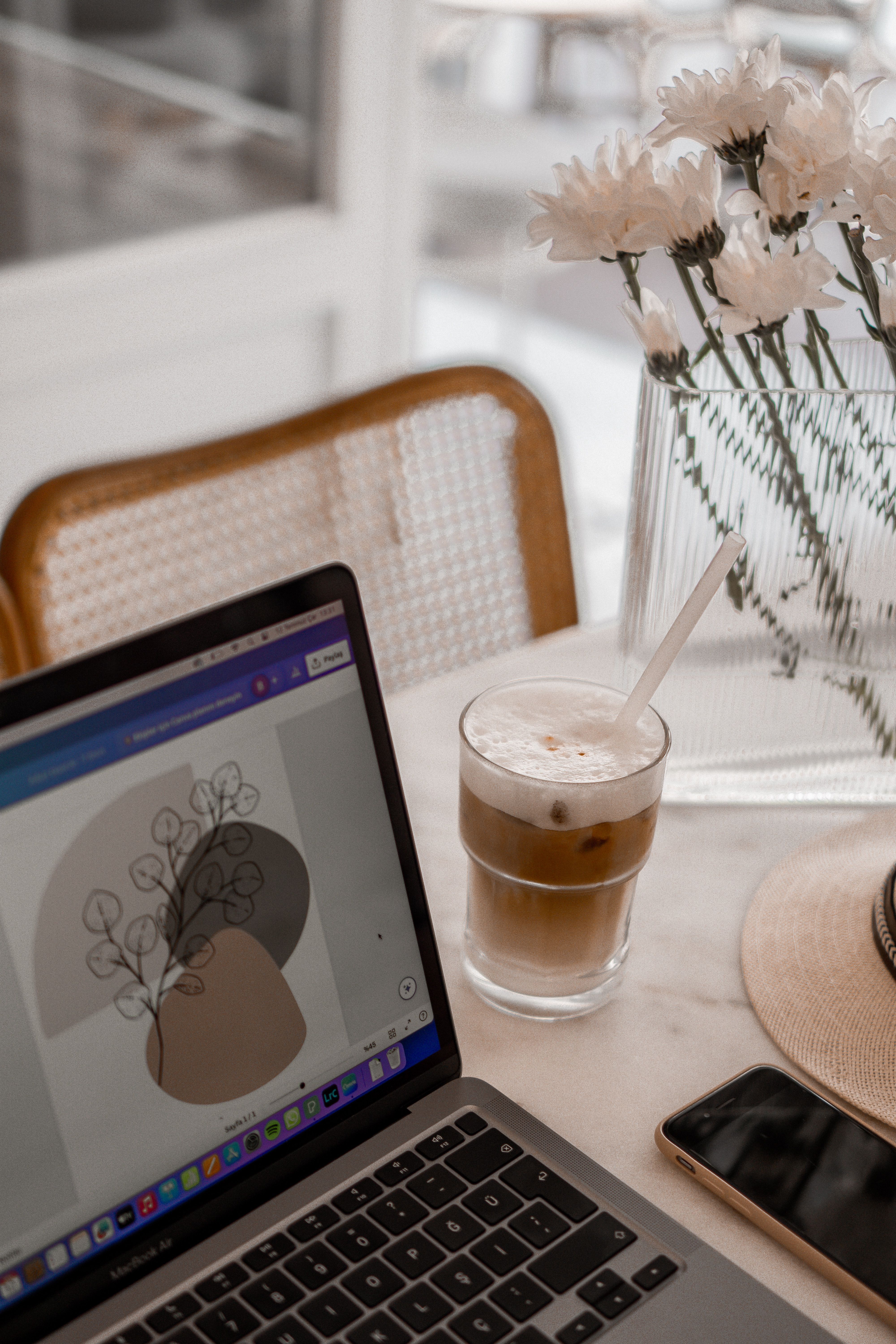 A cozy indoor workspace featuring a laptop, iced coffee, and flowers on a marble table.
