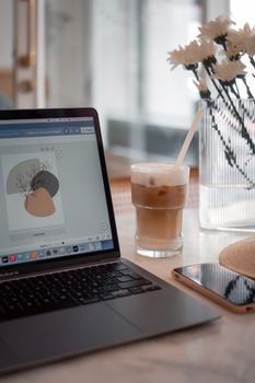 A pleasant workspace featuring a laptop, iced coffee, and flowers on a marble table.