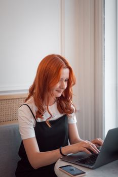 Red-haired woman typing on laptop indoors, focused on work.