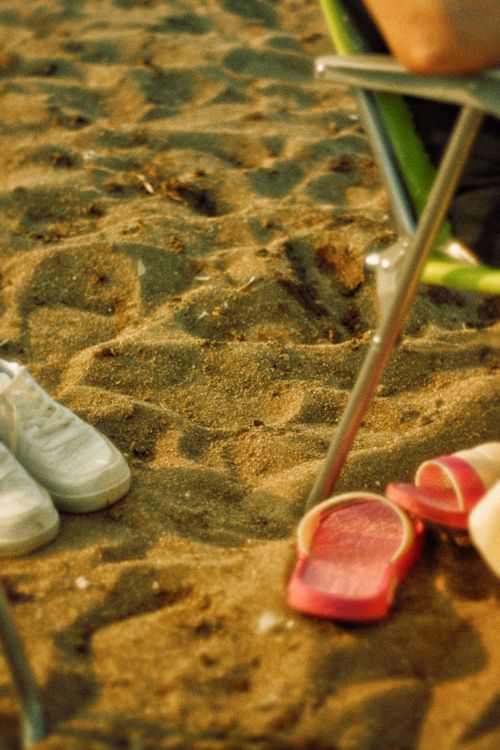 Free A serene beach setting with red flip flops and a green chair, ideal for a relaxing vacation. Stock Photo