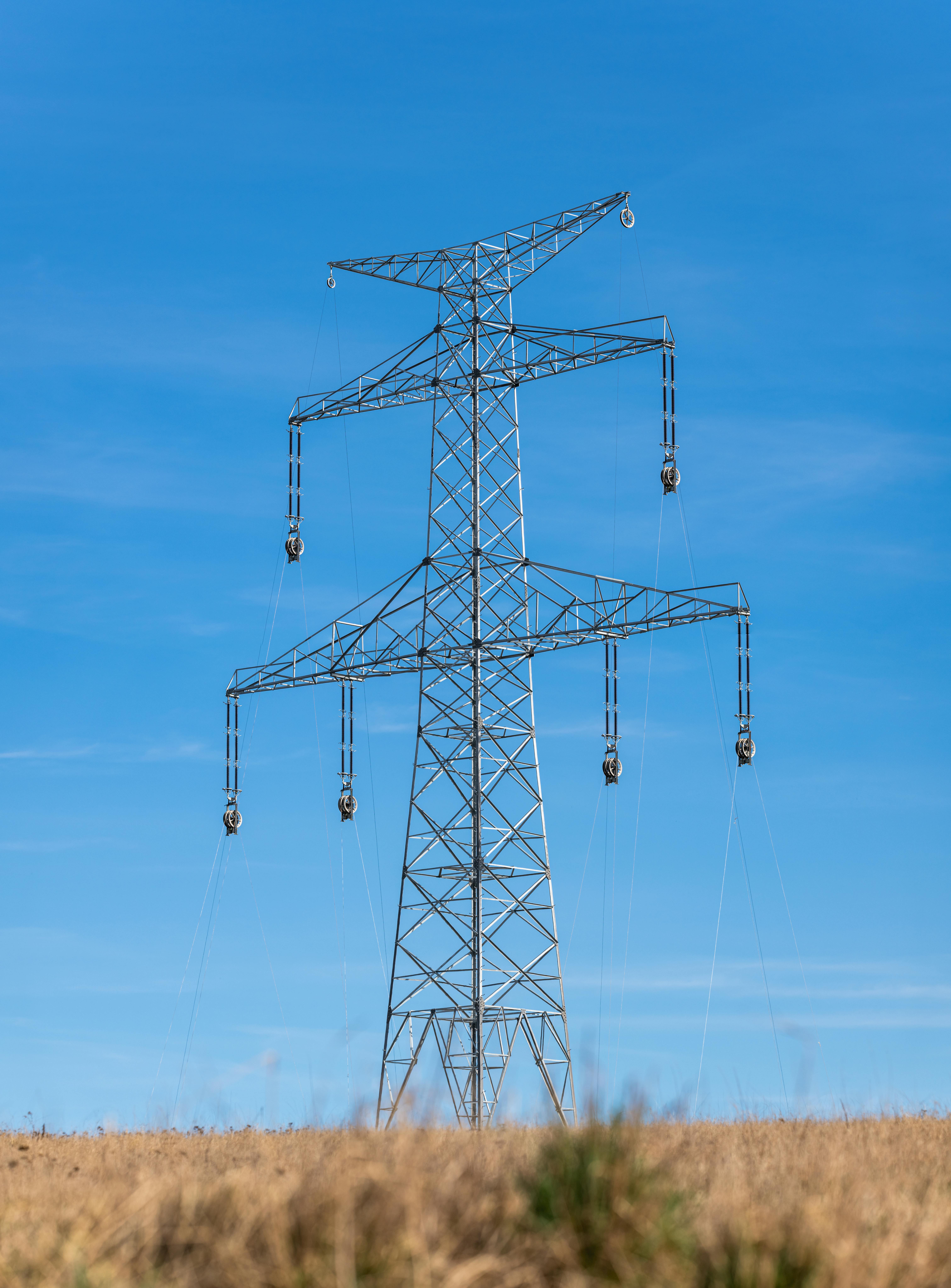 A high voltage transmission tower stands tall in a rural field under a clear sky.