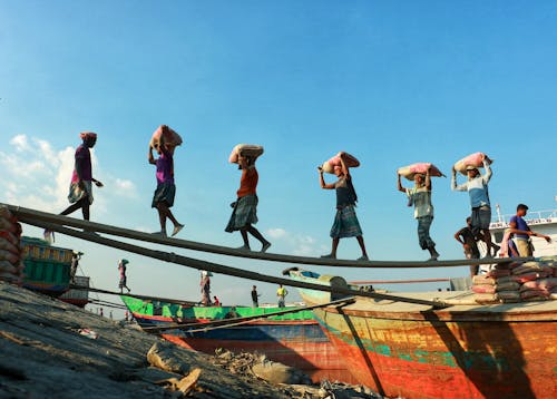 Workers Carrying Bags From Boats to Shore