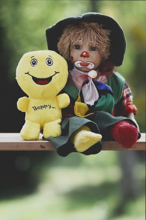 Smiley and Sad Clown Puppets Sitting on a Wooden Plank