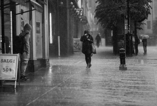Black and white photo of people walking in heavy rain on Bergen streets. Urban atmosphere.