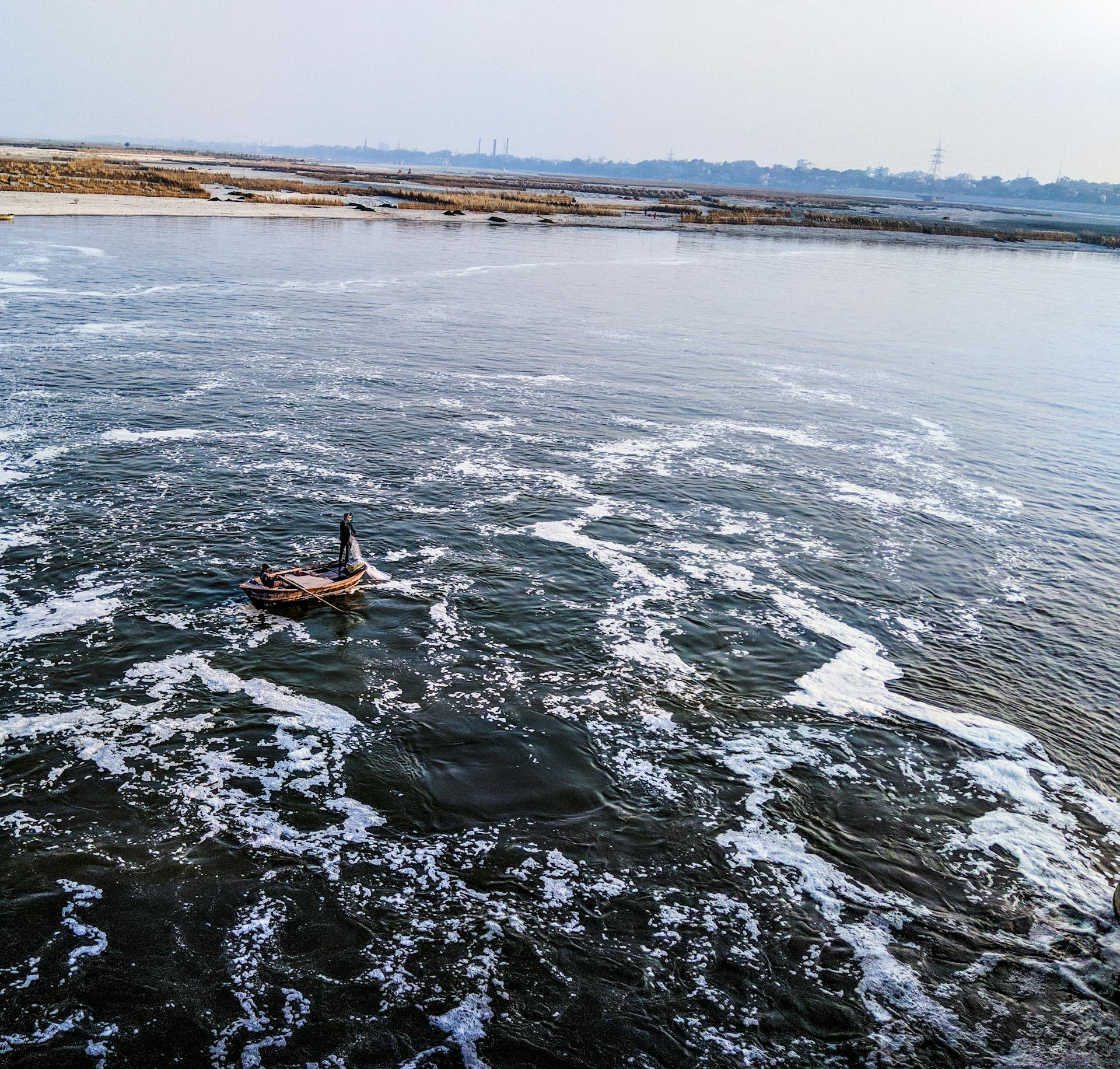 A single boat navigates a river with detailed foam patterns under a clear sky.