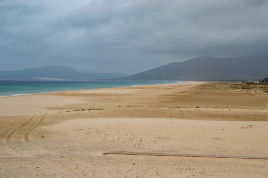 Wide sandy beach under cloudy skies in Tarifa, Spain, offering a serene coastal view.