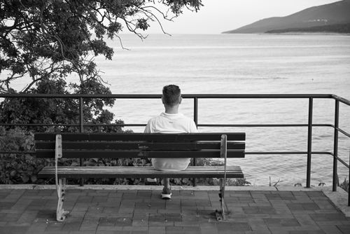 Free A man sits on a bench overlooking a tranquil sea, capturing a peaceful moment at the waterfront. Stock Photo
