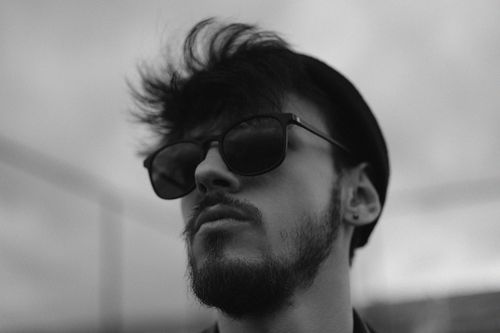 Free Black and white portrait of a man wearing sunglasses and a hat, looking confidently upward. Stock Photo