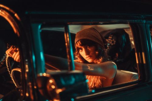 Free A young woman in a beanie poses confidently in a vintage car, illuminated by cinematic teal and orange lighting. Stock Photo