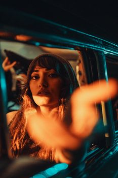 A moody portrait of a woman with bangs reaching out from a car window in warm tones.