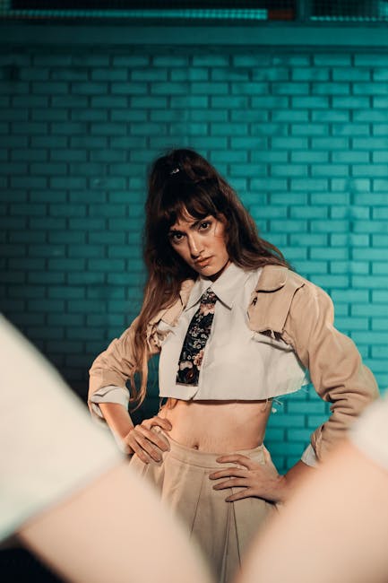 Portrait of a confident woman posing with hands on hips against a teal brick wall.