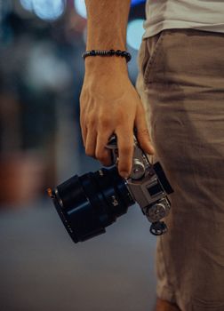 Close-up of a man holding a camera in an urban night setting, casual and artistic.