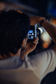 A man takes a night photograph using a camera, highlighting urban lights and atmosphere.