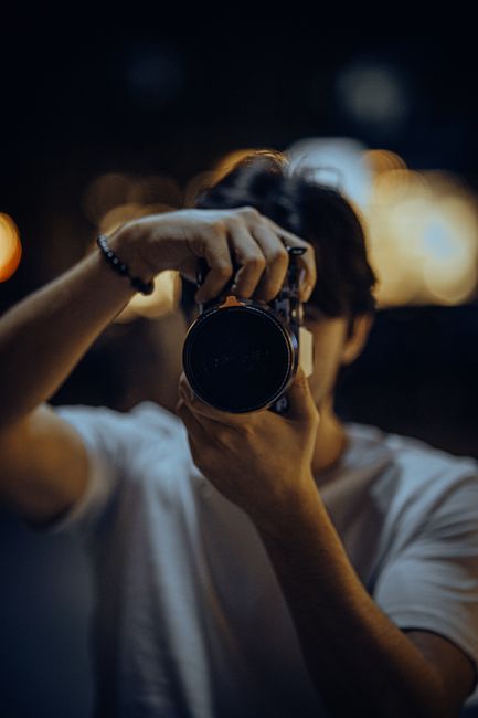 A photographer in a white shirt holding a camera, capturing a moment in low light.