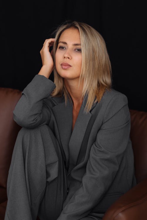 Blonde Woman in Elegant Grey Suit Sitting on a Leather Sofa