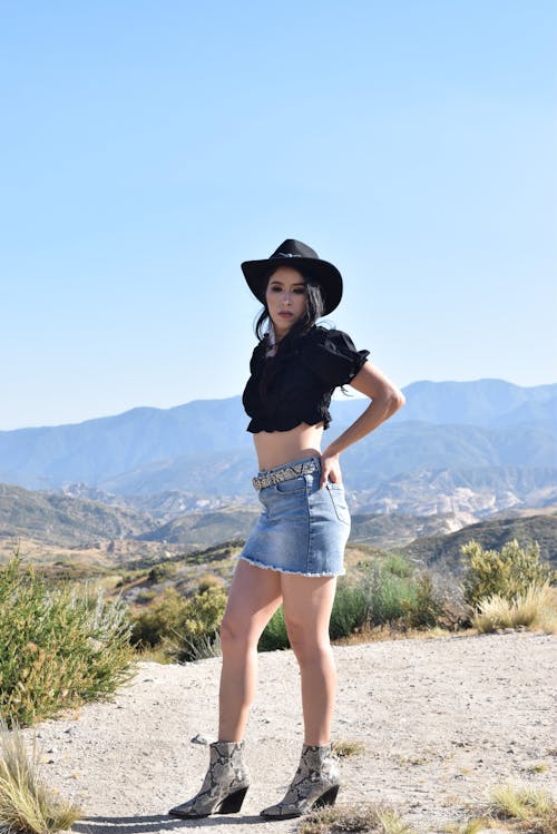 Woman in Cowboy Hat, Ruffled Blouse and Denim Mini Skirt Posing in a Mountain Valley