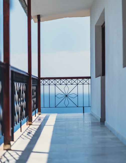 An empty balcony with decorative railings overlooking a tranquil sea under a clear sky.