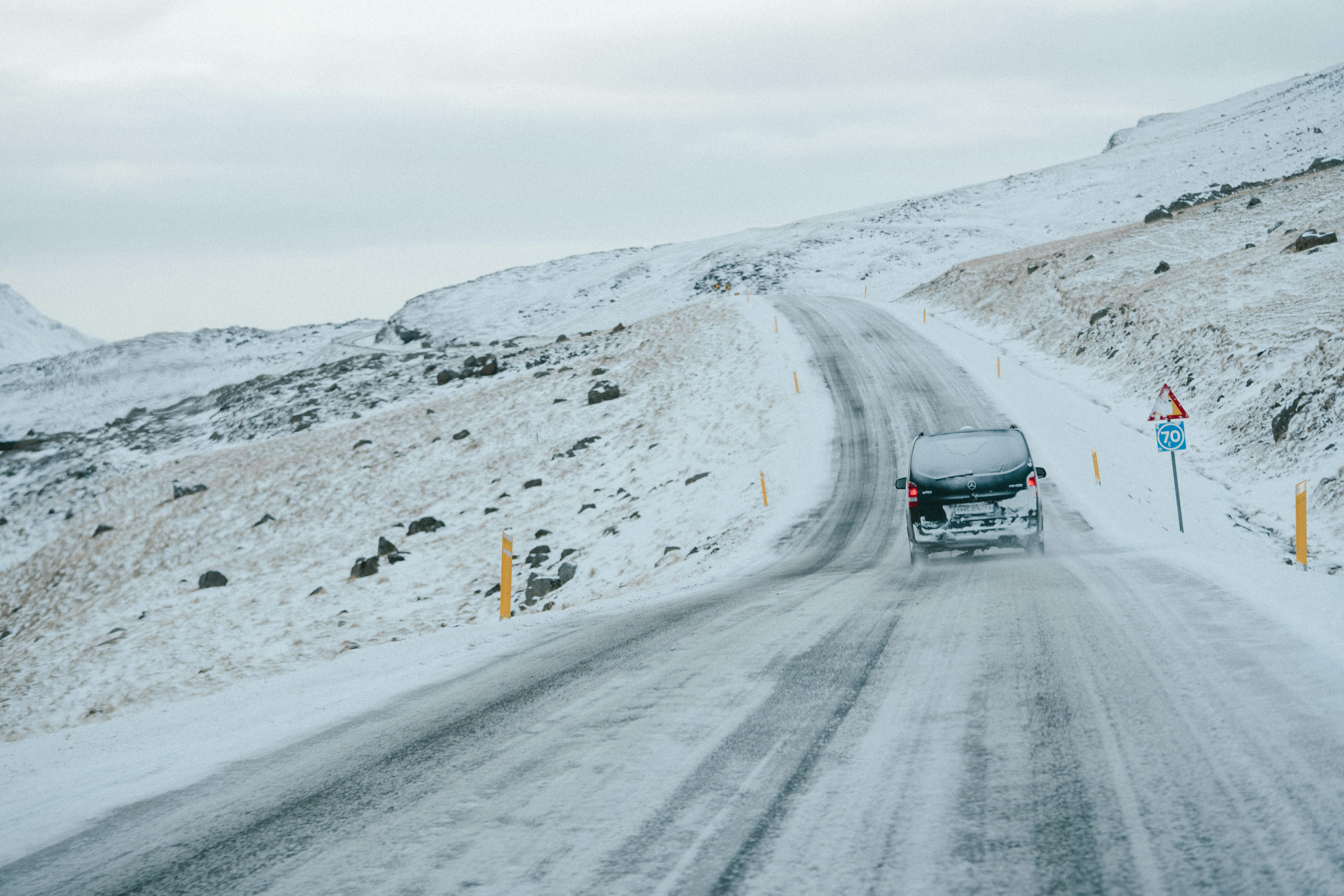 Van traveling on a snow-covered road through a serene mountainous winter landscape.