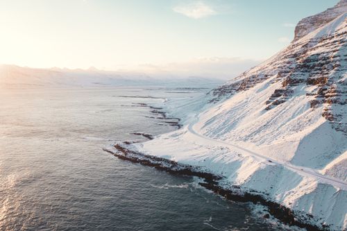 Free Stunning aerial view of a snow-covered coastal mountain at sunrise, showcasing the beauty of winter nature. Stock Photo