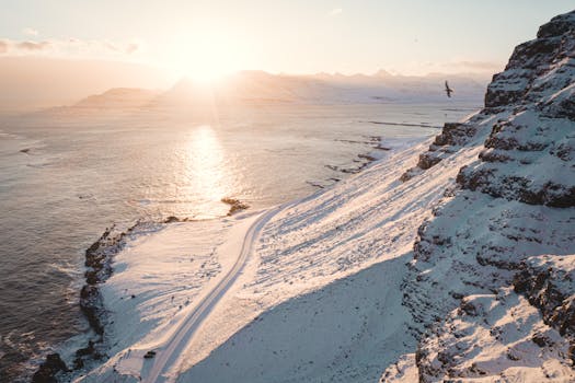 A stunning snowy coastal scene captured at sunrise, highlighting nature's beauty with sunlit sea and mountains.
