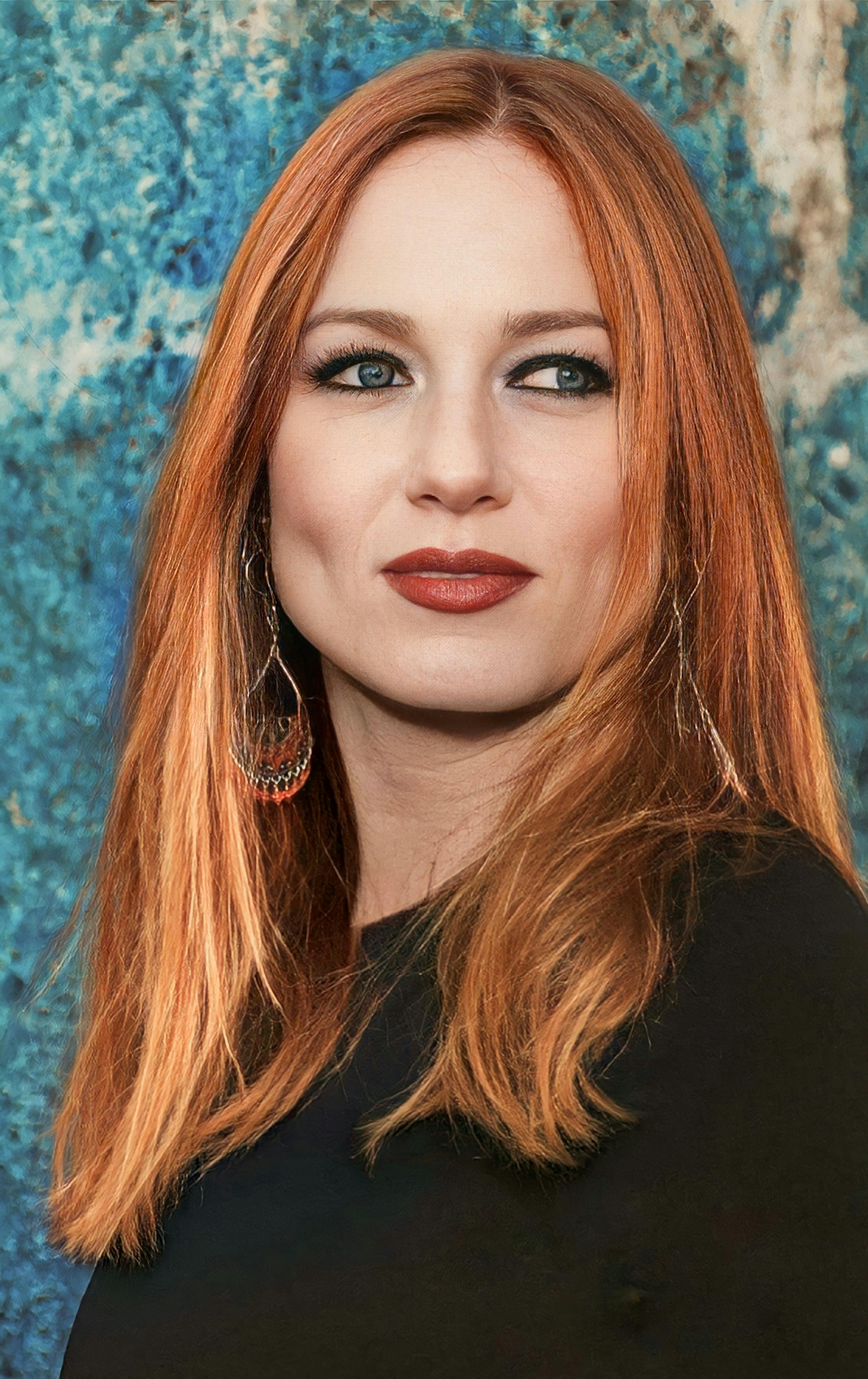 Stunning portrait of a woman with red hair and earrings against a blue background.
