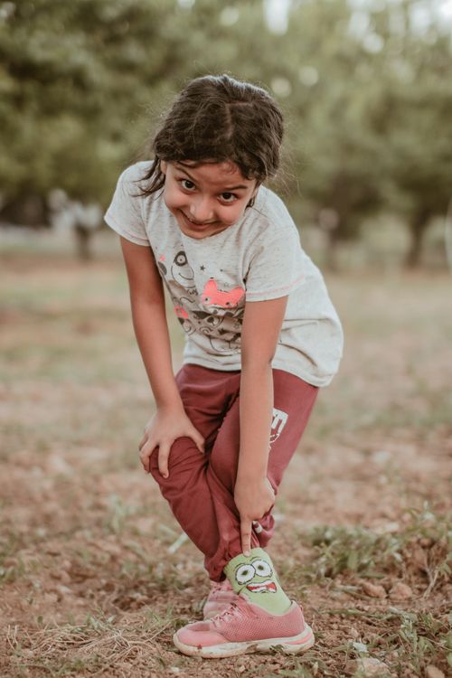 Free Smiling young girl in casual clothes enjoying a playful moment in a grassy outdoor setting. Stock Photo