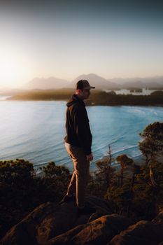 A man stands on a hill overlooking the ocean, embracing tranquility and natural beauty at sunset.