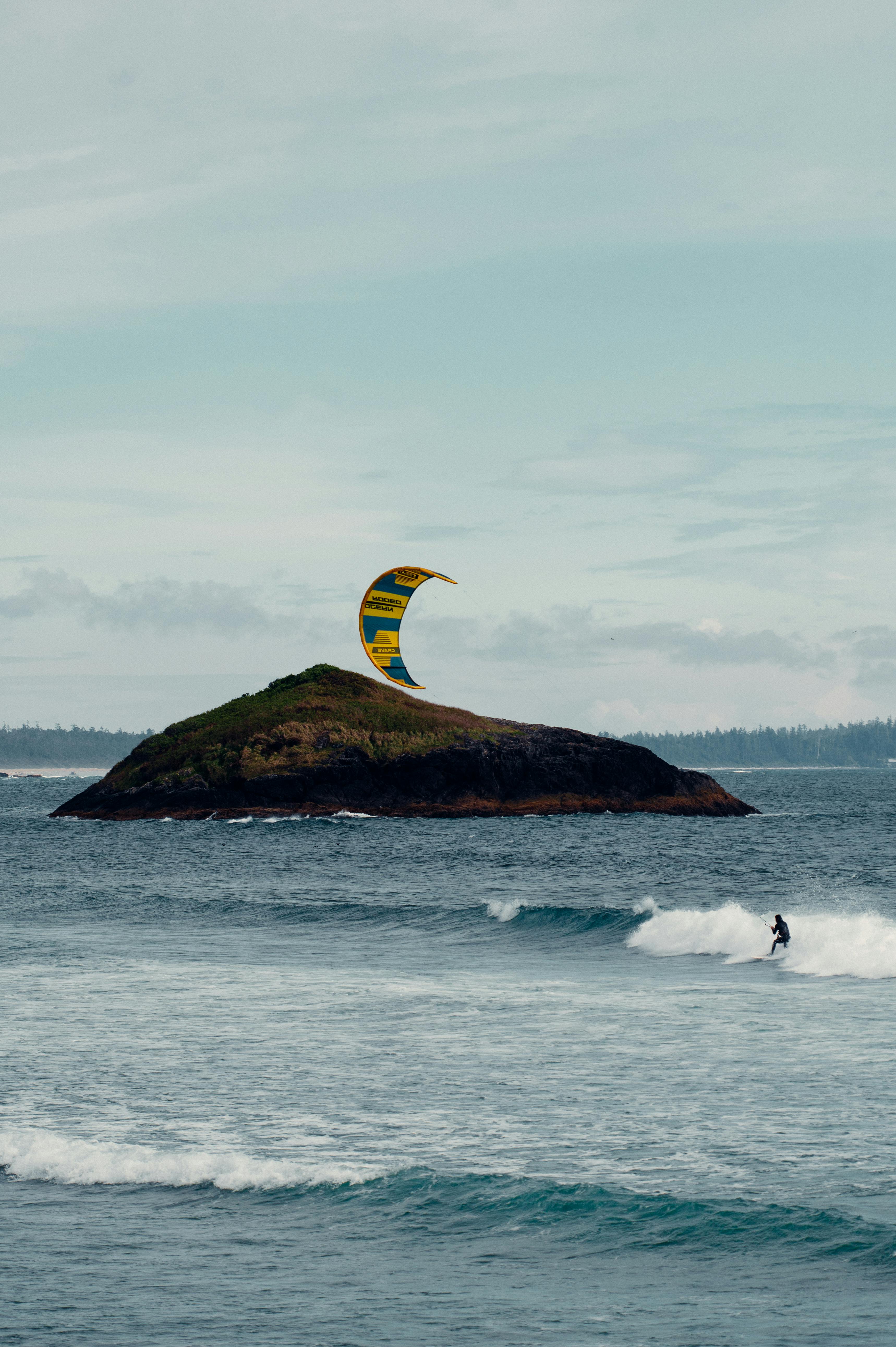 A dynamic kitesurfer rides waves near a remote island, capturing the essence of coastal adventure.