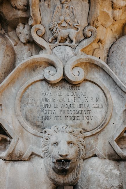 Close-up of a historic Italian fountain with ornate lion relief and engraved text.