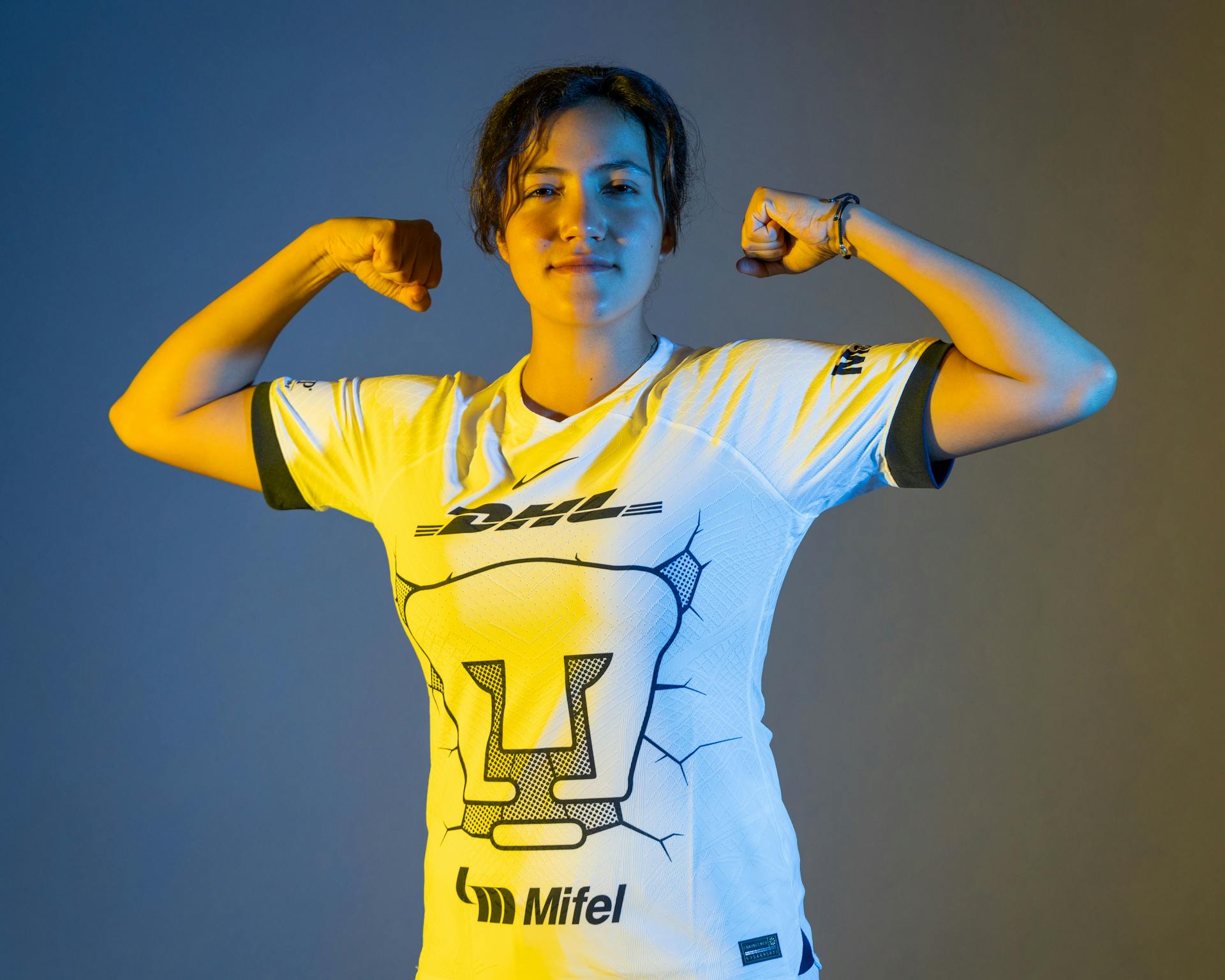 Portrait of a confident sportswoman flexing muscles in a sporty jersey against a gradient background.