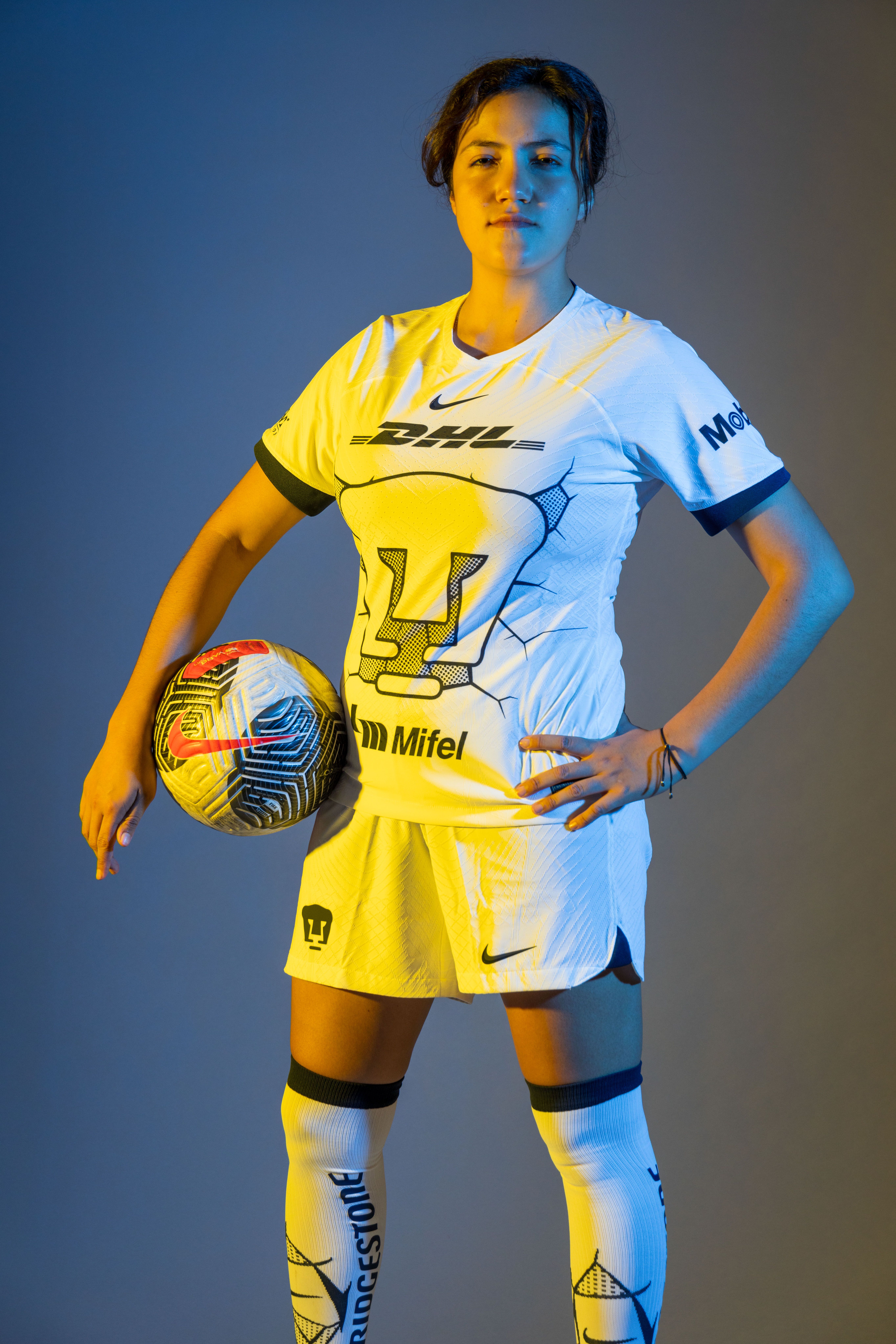 Female soccer player in sportswear posing with a soccer ball in a studio setting.