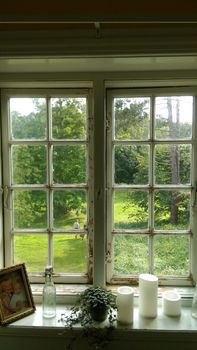 Charming view of a lush garden through rustic window with candles and greenery.