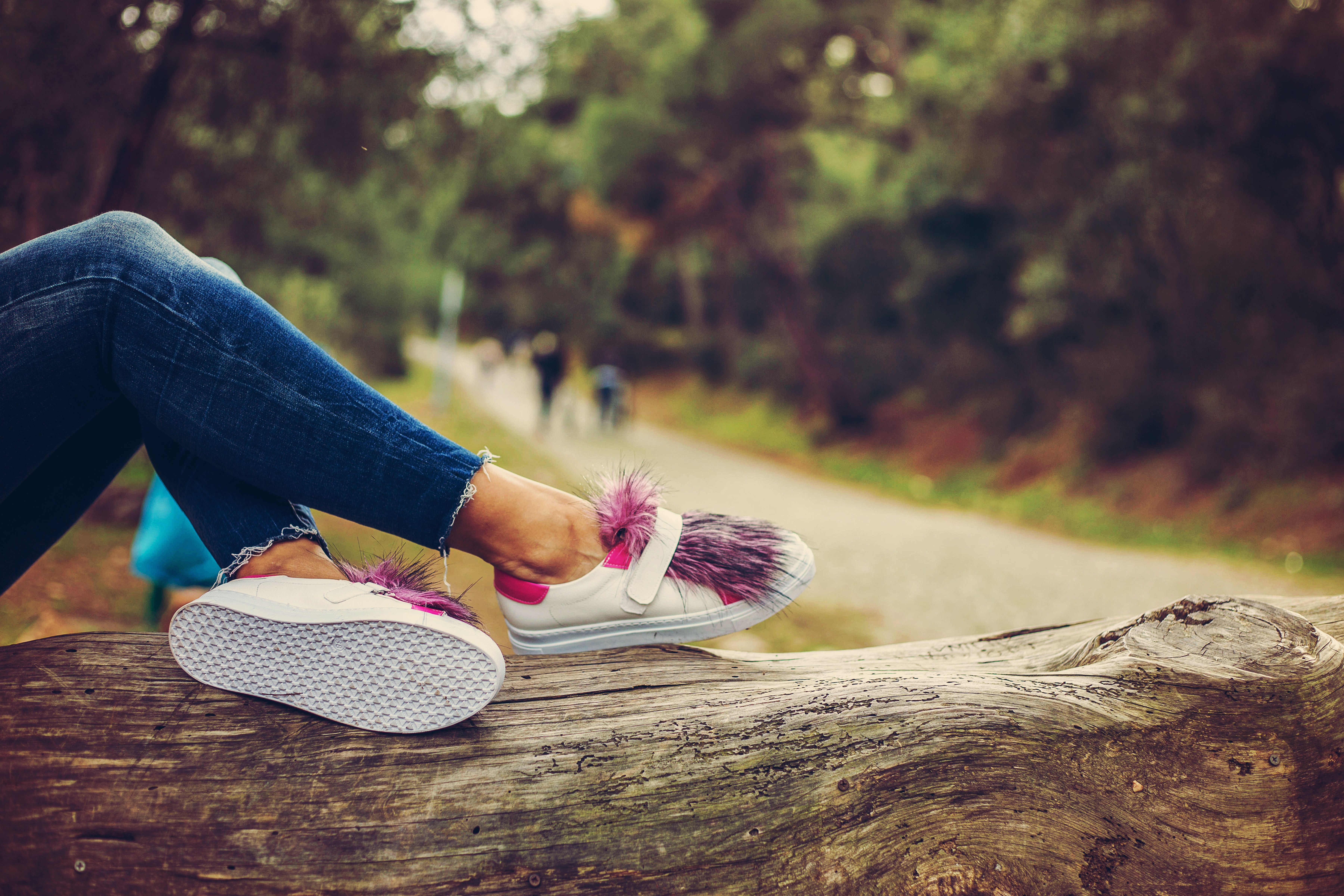 Stylish sneakers with purple fur detail resting on a log in a serene outdoor setting.