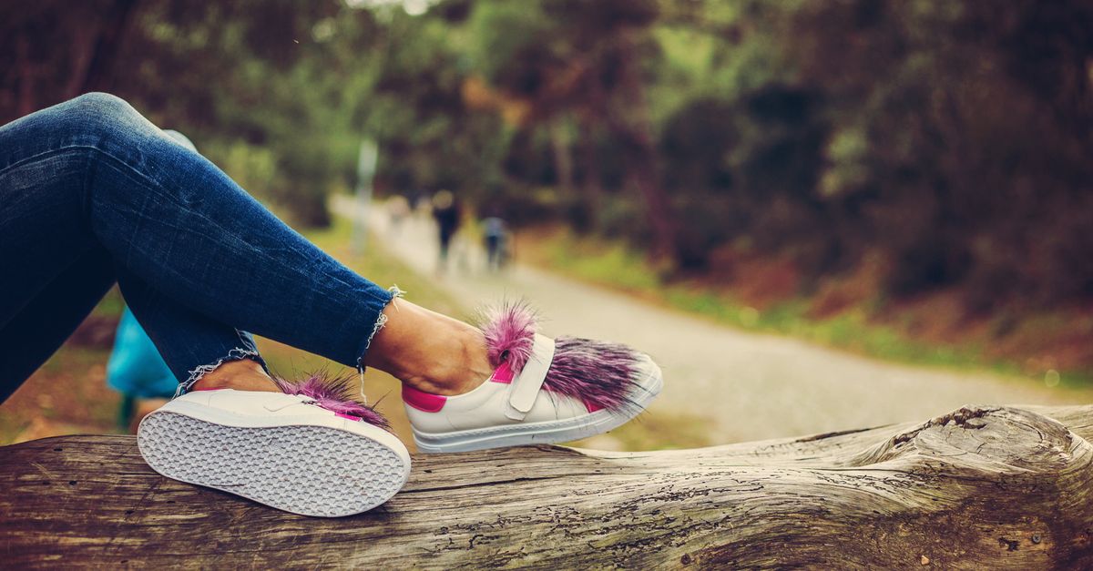 Stylish sneakers with purple fur detail resting on a log in a serene outdoor setting.