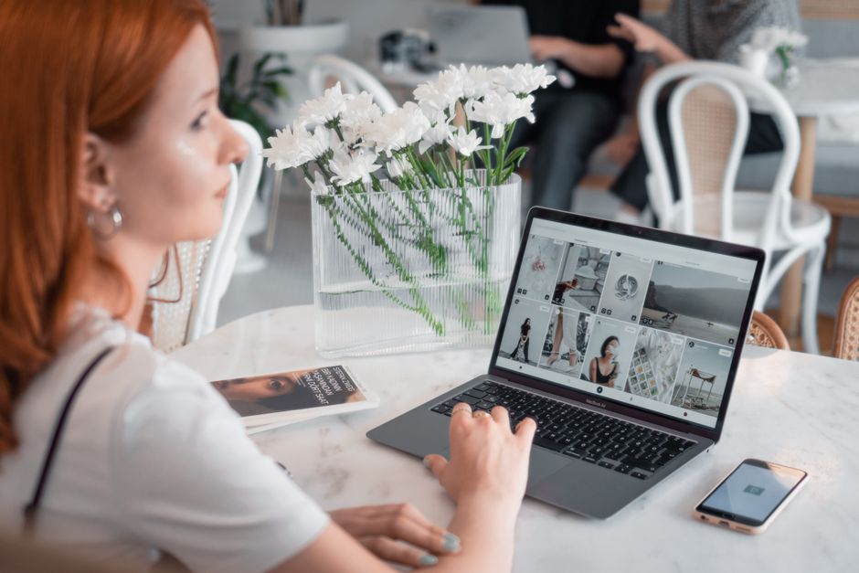 A woman with red hair works on a laptop in a cozy modern cafe, surrounded by stylish decor.
