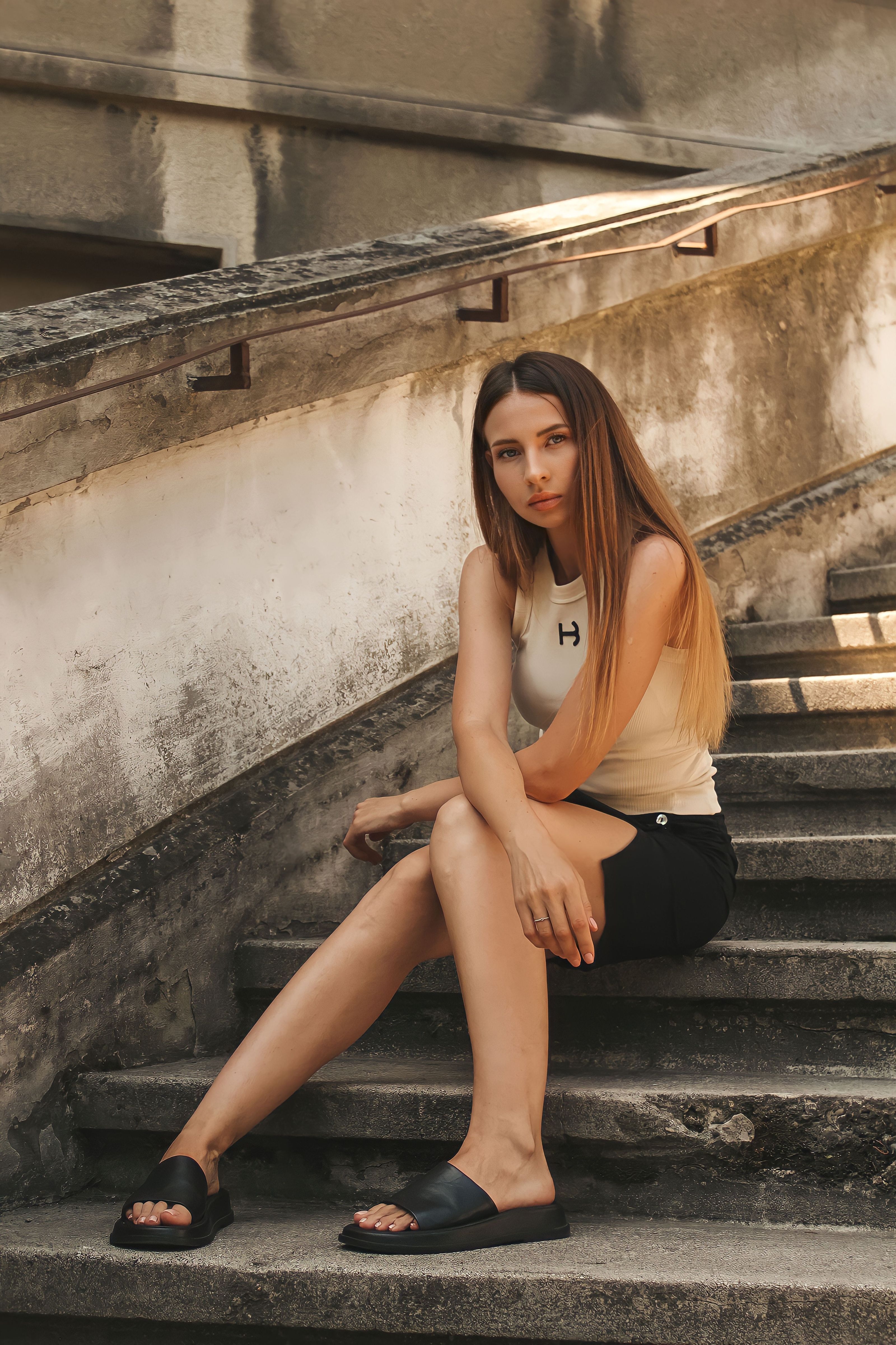 Jovem estilosa com outfit de verão casual sentada em degraus de concreto ao ar livre.