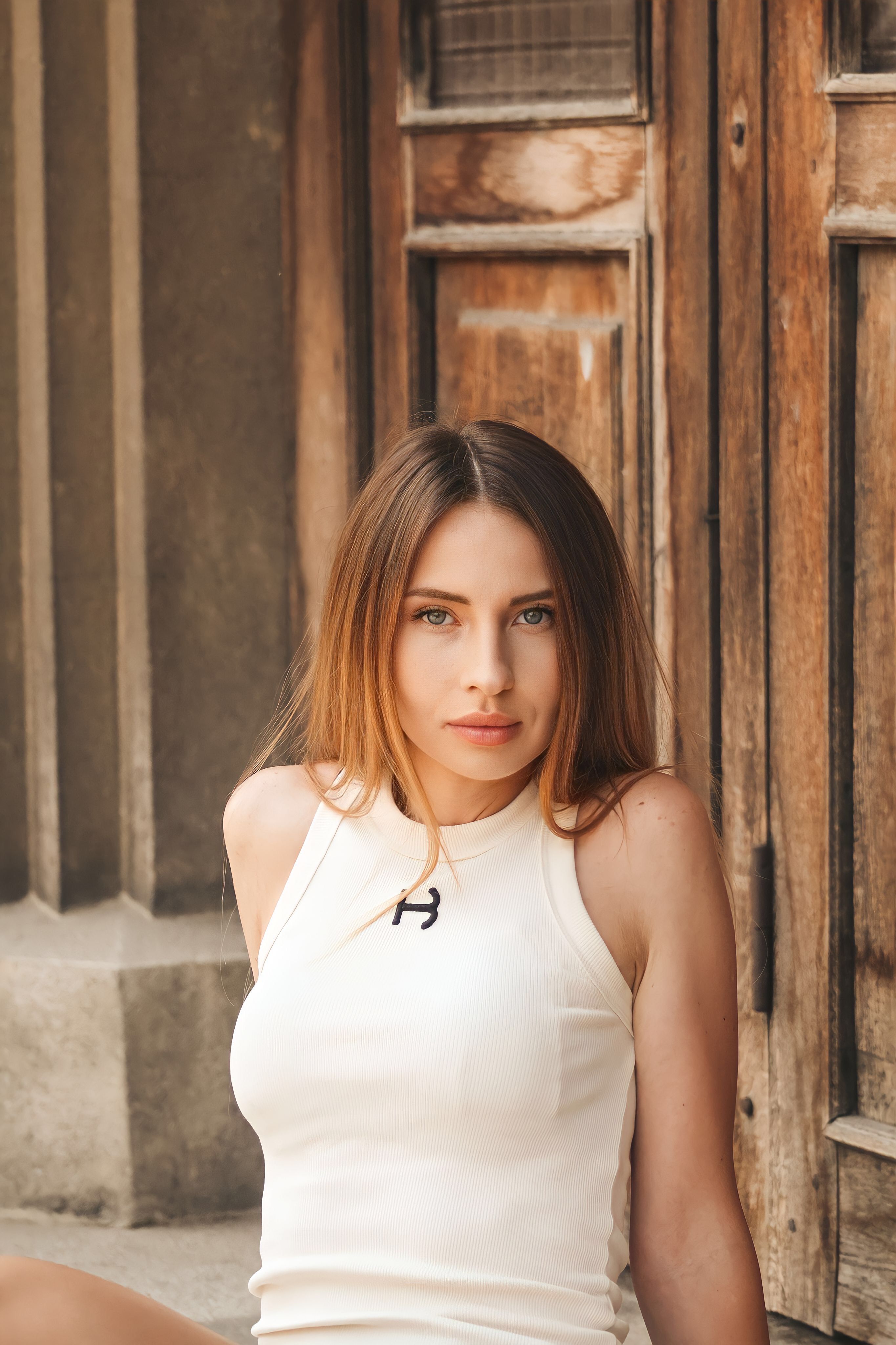 Young woman in tank top sitting against wooden door, showcasing urban style fashion.