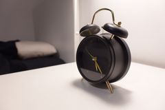 Vintage-style black alarm clock on modern minimalist bedside table in a cozy bedroom.