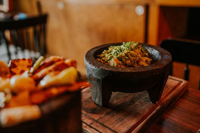Delicious guacamole in a rustic stone bowl on wooden table. Perfect for restaurant menus and food blogs.