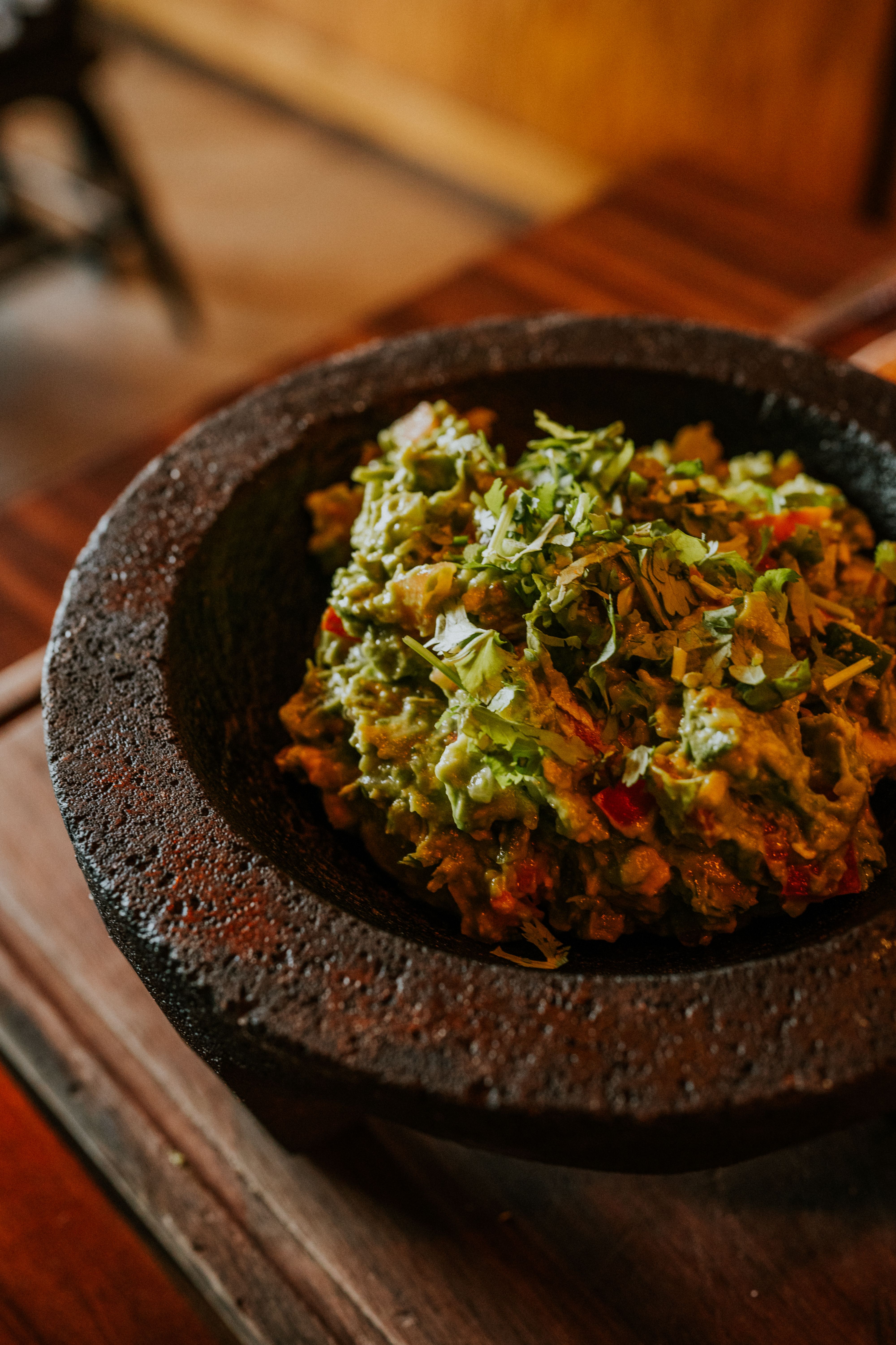 Guacamole frais parsemé de coriandre dans un mortier de pierre posé sur du bois