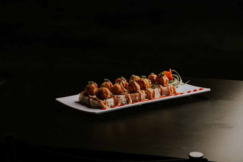 Gourmet sushi roll with crispy tempura topping, garnished with vegetables on a black background.